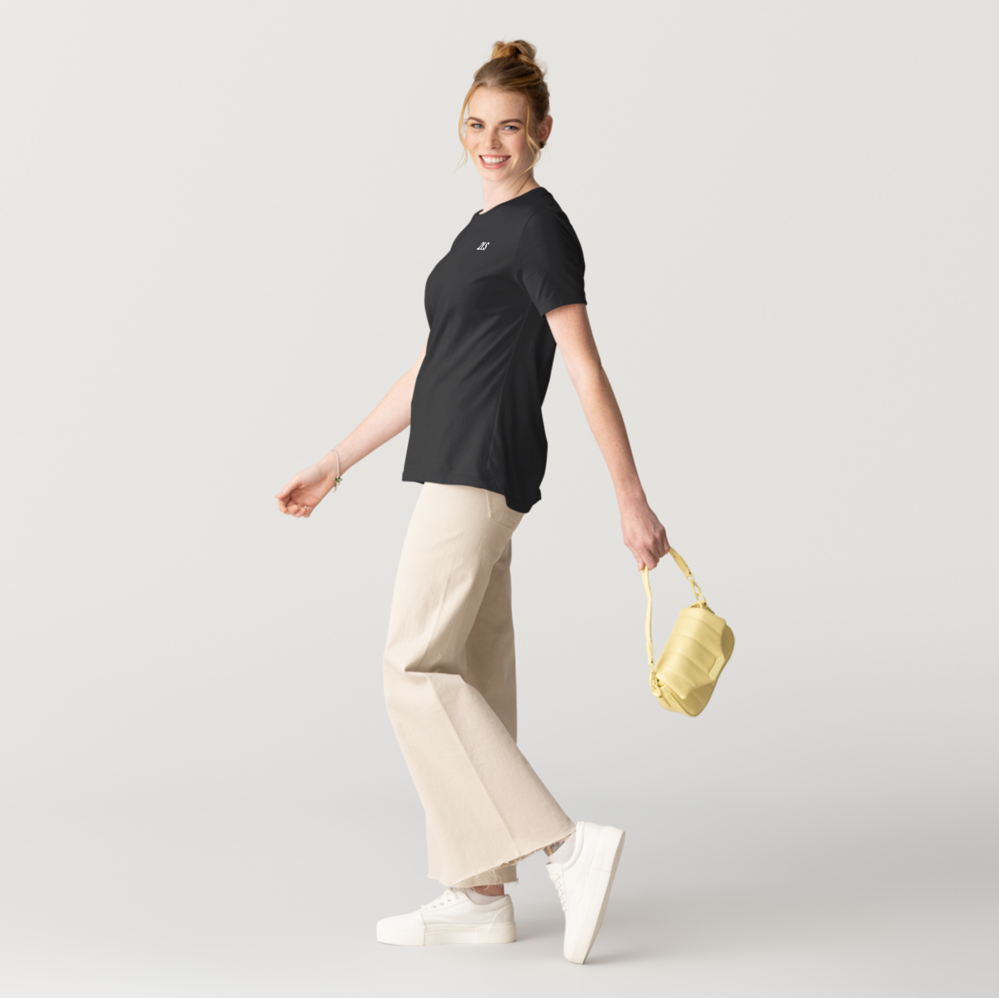 Woman wearing a black t-shirt and beige pants, holding a yellow handbag on a light gray background 2lowsierra 2LS