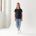 Person wearing a black t-shirt and light blue jeans standing in a minimalistic  2lowsierra 2ls room.
