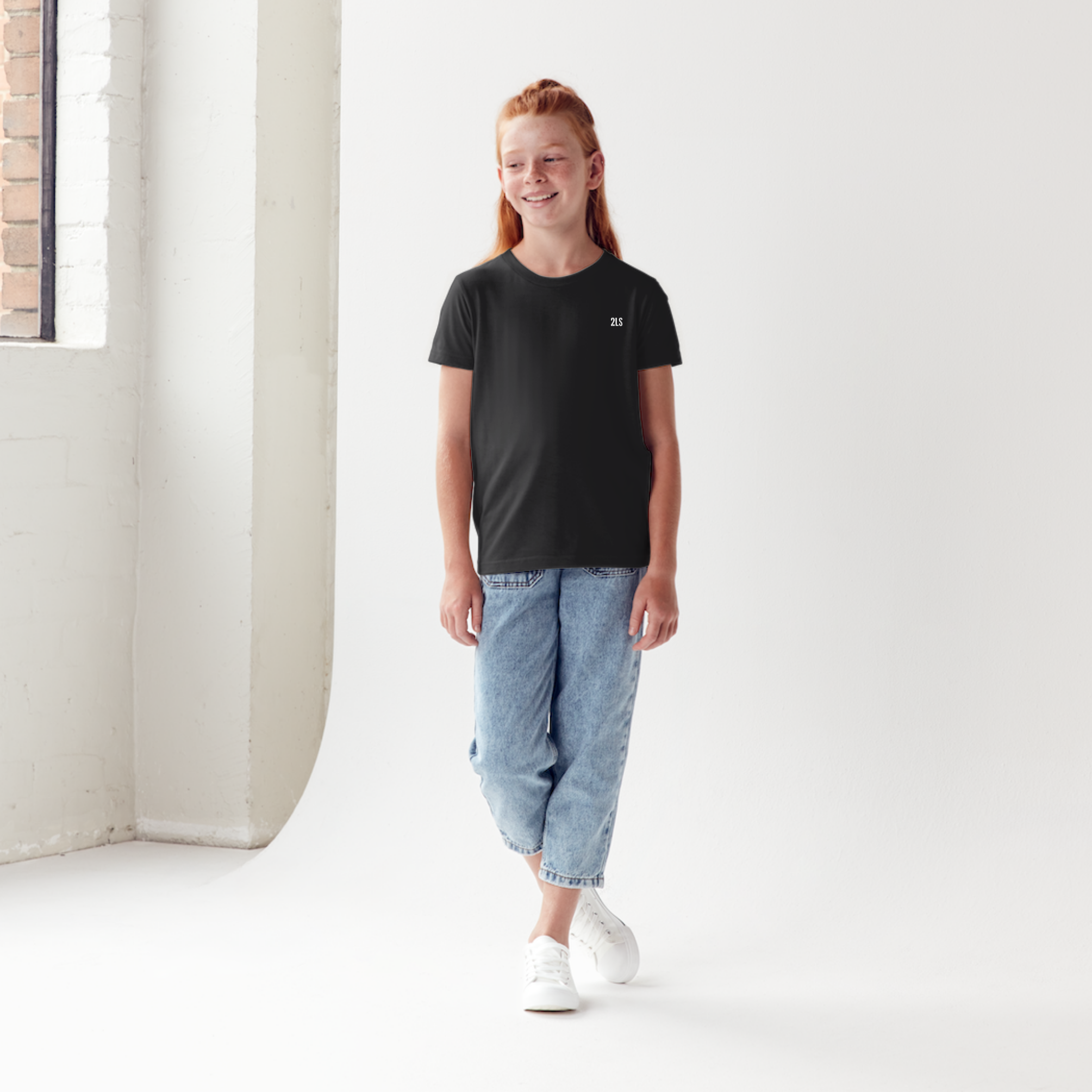 Person wearing a black t-shirt and light blue jeans standing in a minimalistic  2lowsierra 2ls room.